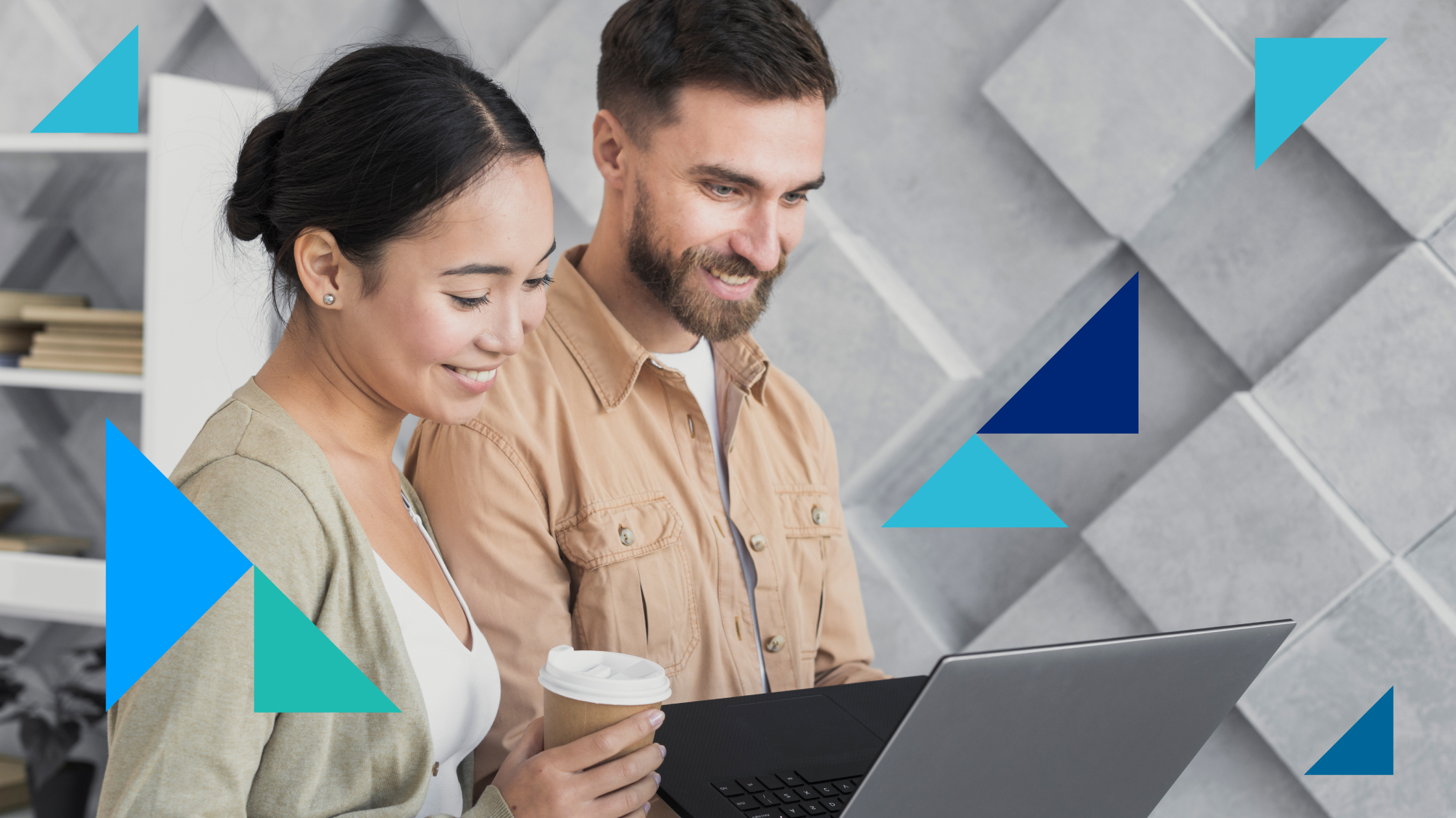 A man and a woman look at a laptop together. They're both smiling and the man holds the laptop while the woman holds a cup of takeaway coffee.