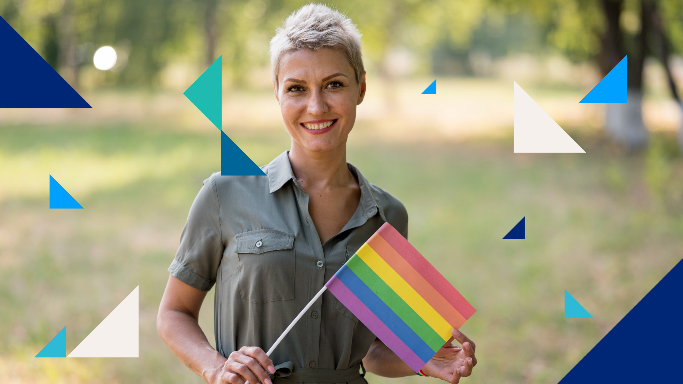 Une femme à la coupe de cheveux pixie sourit en tenant un petit drapeau de la fierté arc-en-ciel.